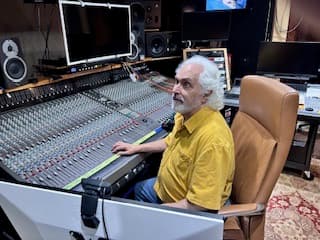 Ross Winetsky seated at his mixing console, one hand on the controls, surrounded by studio monitors and racks of outboard gear.